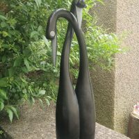 Carved stone sculpture depicting two stylized swans or herons with elongated necks, dark stained finish