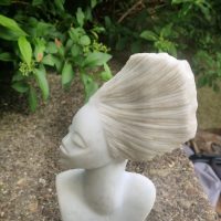 White composite stone bust sculpture of a woman with elaborate swept-back hair